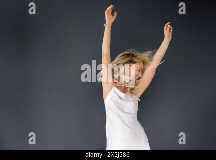 Joyful woman in white dress dancing on black background Stock Photo