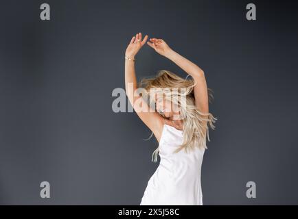 Joyful woman in white dress dancing on black background backgrou Stock Photo