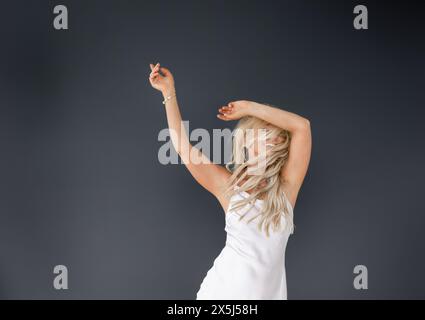 Joyful woman in white dress dancing on dark background Stock Photo