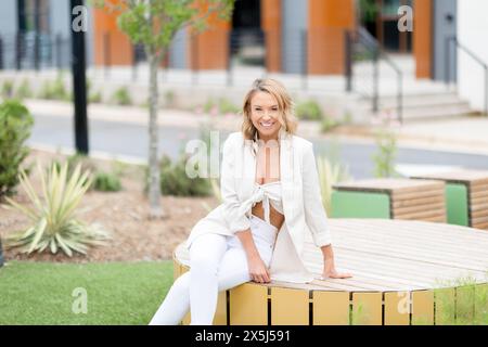 Cheerful woman sitting on bench in urban park Stock Photo