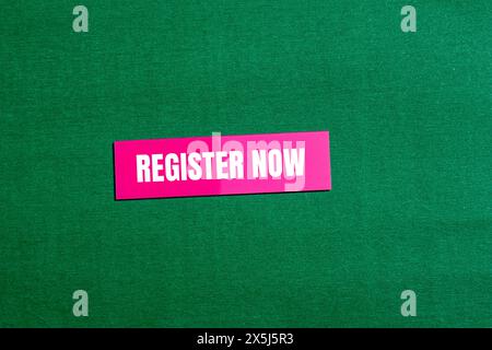 Register now words written on pink paper sticker with green background. Conceptual register now symbol. Copy space. Stock Photo