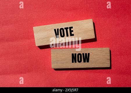 Vote now words written on wooden blocks with red background. Conceptual vote now symbol. Copy space. Stock Photo