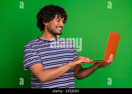 Photo portrait of young senior level programmer indian guy works online using laptop write code isolated on green color background Stock Photo