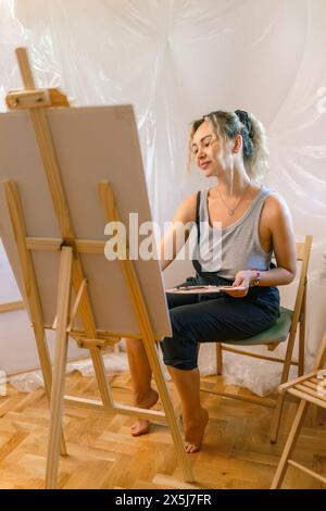 Satisfied female artist posing near new picture next to easel Stock Photo