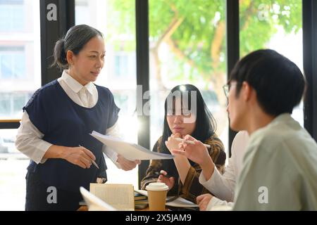 Friendly senior professor helping group of students during class at university Stock Photo