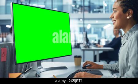 Diverse Corporate Office: Beautiful Black Female IT Technician Using Desktop Computer with Green Chroma Key Screen. Creative Software Engineer Work on eCommerce Project Marketing, Development Stock Photo