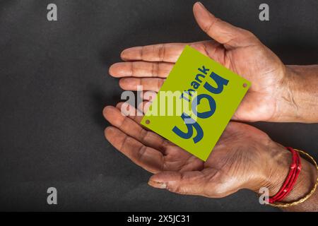 Thank you card in the hands of an old woman on a black background. Close up Stock Photo