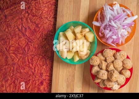 Various vegetable dishes ready for cooking on a wooden cutting board. Three bowl of meal maker and sliced potatoes and onions. Stock Photo