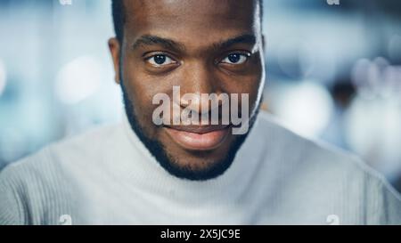 Close-up Portrait of Handsome Black Man with Deep Brown Eyes, Trimmed Beard, Wearing Stylish Turtleneck, Smiles Charmingly. Attractive Authentic African American Gentleman Looks up at the Camera Stock Photo