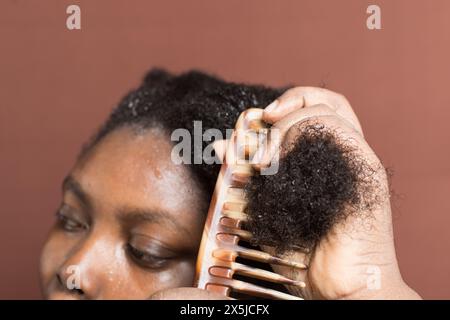 Combing black afro curly hair with shrinkage, using a wide tooth comb to detangle wet Type 4c hair Stock Photo