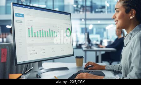 Corporate Office: Black Female IT Technician Using Desktop Computer with Big Data Statistics, Graphs. Smiling Creative Software Engineer Work on eCommerce Project Marketing, Development. Stock Photo