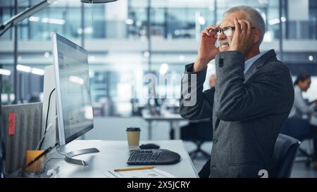 Senior White Male Corporate Office Worker Works on Computer, Feels Sudden Pain, Headache, Migraine. Accountant Feeling Project Pressure, Stress, Massages Her Head, Temples Stock Photo