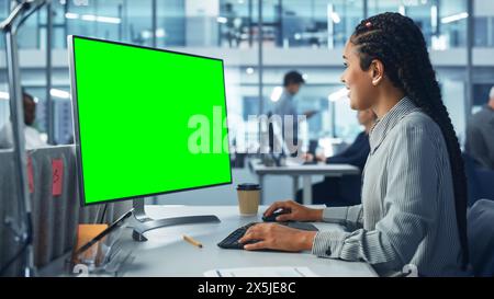 Diverse Corporate Office: Beautiful Black Female IT Technician Using Desktop Computer with Green Chroma Key Screen. Creative Software Engineer Work on eCommerce Project Marketing, Development Stock Photo