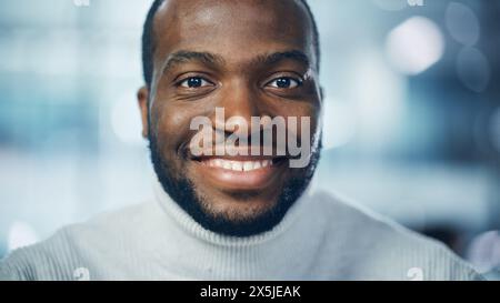 Close-up Portrait of Handsome Black Man with Deep Brown Eyes, Trimmed Beard, Wearing Stylish Turtleneck, Smiles Charmingly. Attractive Authentic African American Gentleman Looks up at the Camera Stock Photo
