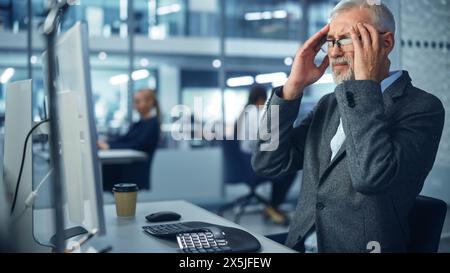 Senior White Male Corporate Office Worker Works on Computer, Feels Sudden Pain, Headache, Migraine. Accountant Feeling Project Pressure, Stress, Massages Her Head, Temples Stock Photo