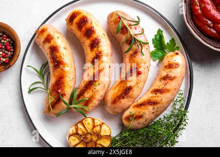 Grilled sausages with tomato sauce and herbs served on plate. Roasted homemade wurst sausages on plate. Stock Photo