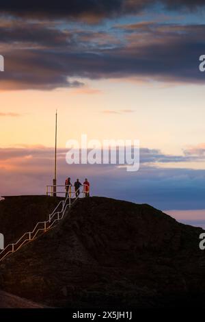 Evening light over people standing on top of Chapel Rock at the end of the breakwater in Bude in Cornwall in the UK. Stock Photo