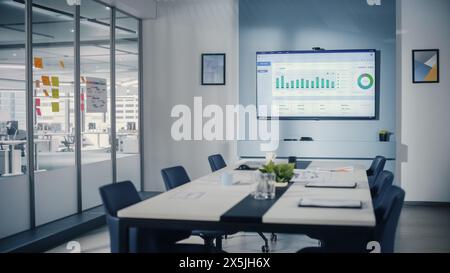 Modern Empty Meeting Room with Big Conference Table with Various Documents and Laptops on it, on the Wall Big TV with Big Data Analysis, Charts and Infographics. Contemporary Designed Work Environment Stock Photo