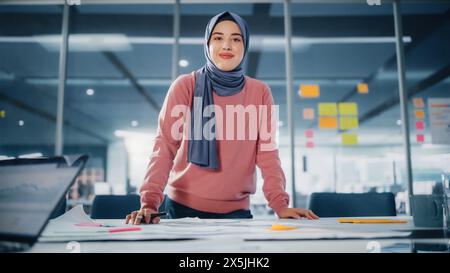 Modern Office: Portrait of Muslim Businesswoman Wearing Hijab Works on Engineering Project, Does Document and Blueprints Analysis. Empowered Digital Entrepreneur Works on e-Commerce Startup Project Stock Photo