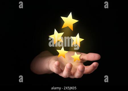 Man holding virtual stars on black background, closeup. Customer satisfaction score Stock Photo