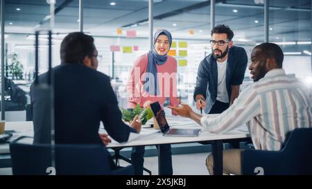 Diverse Modern Office: Muslim Businesswoman Wearing Hijab and Stylish Hispanic Entrepreneur Lead Business Meeting, Use Laptop, Talk, Brainstorm with Managers. Young Professionals on e-Commerce Project Stock Photo