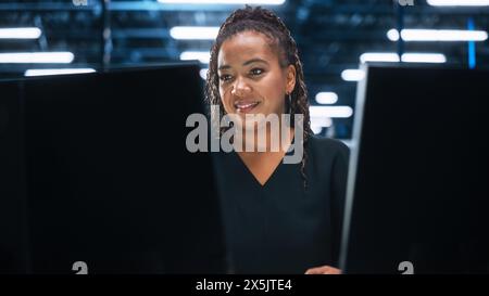 Mature CEO Specialist Working on Computer in Night Creative Office Environment. Beautiful Diverse Multiethnic Female Project Manager is Using Two Monitors with Pleasure Smile Stock Photo