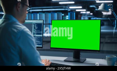 Confident male Data Scientist Works on Personal Computer with Green Screen Mock Up in Big Infrastructure Control and Monitoring Room with Neural Network. Man Engineer in an Empty Office Stock Photo