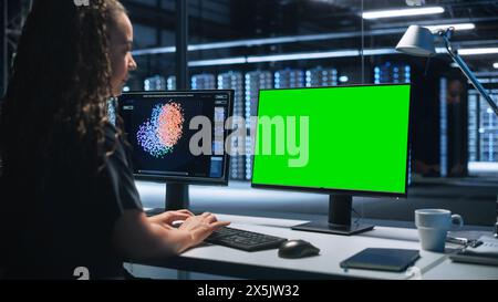 Smart Female IT Programer Working on Desktop Green Mock-up Screen Computer in Data Center System Control Room. Professional Programming Sophisticated Code in a High Tech Development Laboratory. Stock Photo