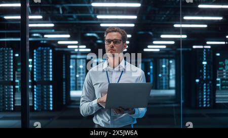 Caucasian Young Male IT Specialist Using Laptop, Standing in Data Center. Skilful Man Works on Web Services. Cloud Computing, Server Analytics, Cyber Security Maintenance Stock Photo