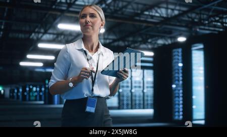 Data Center Female e-Business Entrepreneur Use Tablet Computer with Pleasure Smile. Information Technology Engineer and System Administrator work in Big Cloud Computing Server Farm. Stock Photo