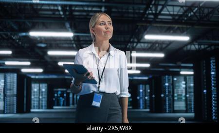 Portrait of a Young Creative Caucasian Female with Blonde Hair Using a Tablet Computer in Evening Office. Beautiful Independent Woman is Walking Through the Office and Looking Away Stock Photo