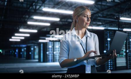 Concentrated Businesswoman or Manager Using Laptop Computer, While Standing in Dark Office or Hall and Working on Financial, Business and Marketing Projects. Business Concept Stock Photo