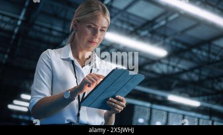 Young Caucasian Female Employee Uses Tablet Computer in System Control Monitoring Center at Night. Evening Office In the Background. Cyber Security and Network Protection Concept Stock Photo