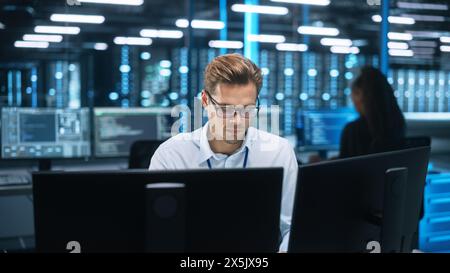 IT Specialist Works on Two Personal Computer at the Software Program with Coding Language Interface. In the Background Technical Room of Data Center with Professional Working Stock Photo