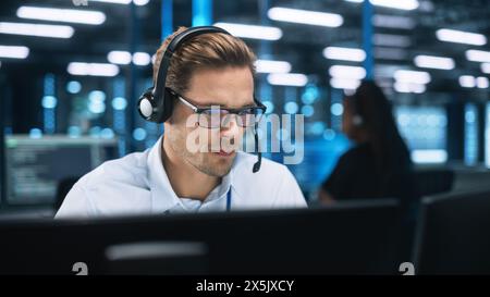 Busy Technical Customer Support Specialist is Talking on Headset while Working on a Computer in a Call Center Control Dark Room During the Evening. Customer Service Concept Stock Photo