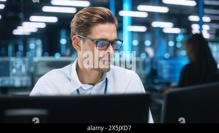 Server Farm Cloud Computing Facility with Male Maintenance Administrator Working During the Evening. Cyber Security and Network Protection. IT Specialist Uses Computer in Data Center. Stock Photo