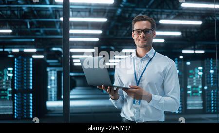 Late at Night in Private Office Male Businessman Works on a Laptop Computer. He Look at the Camera with Smile. Data Protection Engineering Network for Cyber Security. Business Concept Stock Photo