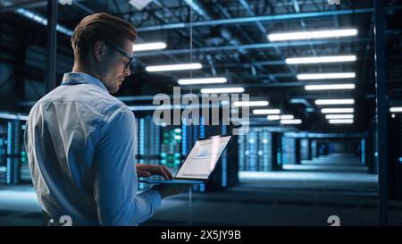 Data Center Male It Specialist Using Laptop while Working on Computer. Information Technology Professional. Server Farm Cloud Computing and Cyber Security Maintenance Concept Stock Photo