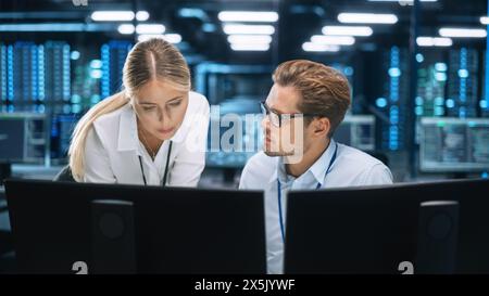 Businessman Uses Desktop Computer, while Consults with Female Project Manager about work issues In the Big Corporate Firm Office at the Background. Businesspeople concept Stock Photo