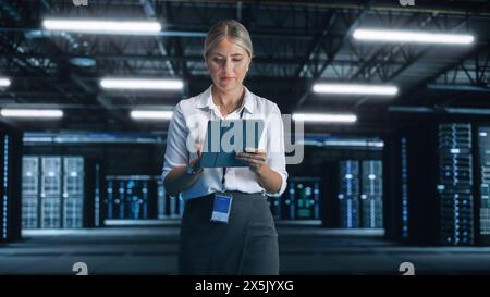 Blonde IT Specialist Using Tablet Computer in Data Center, Walking on a Bridge Overlooking Big Server Farm Cloud Computing Facility. Businesswoman, e-Business Entrepreneur Stock Photo