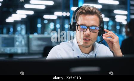 Man Operator in Customer Support Service Center Talking with Client During the Evening. Male Using Computer And Speaking To Customer On The Call During Working At The Office Stock Photo