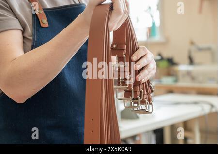 Close-up of a Caucasian woman's hands making genuine leather belts in a workshop.  Stock Photo