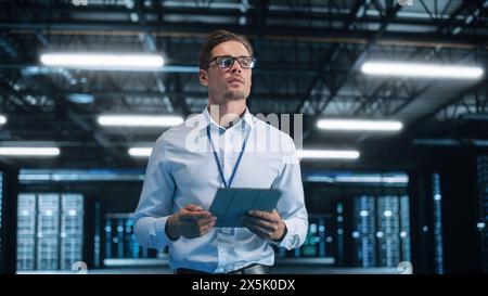 Portrait of IT Specialist Using Tablet Computer in Data Center. Male System Administrator Working with Big Server Farm Cloud Computing Facility. Cyber Security, Network Protection Stock Photo