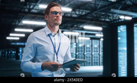 Male Engineer Programs Something while Holding Tablet Computer in His Hands. He Works in a Dark Modern High-Tech Office. High-Speed Data Transfer and Smooth Server Operation, Analytics, Statistics Stock Photo