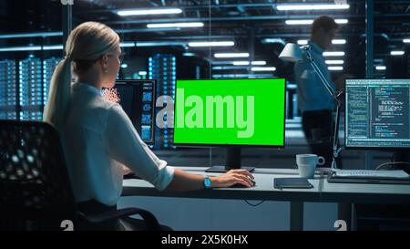 Confident Female Data Scientist Works on Personal Computer with Green Screen Template in Big Control and Monitoring Room. Ambitious Programming Engineer Using Chroma Key to Write Code in Office Room. Stock Photo