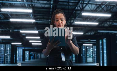 Female Engineer Programs while Holding Tablet Computer and Typing at the Screen. She Works in a Dark Modern High-Tech Office. High-Speed Data Transfer and Smooth Server Operation Concept Stock Photo