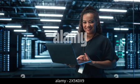 Black Female Chief Technology Office Using Laptop Computer, Standing in Big Office Data Center. System Administrator working with SAAS, Cloud Web Services. E-Business Digital Entrepreneur concept Stock Photo