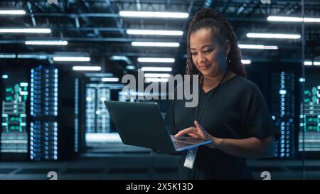 Portrait of Black Female Specialist Using Laptop in Big Data Center. Managing Director Working Attentively. Technology Science Breakethrough. Progress and Innovation concept Stock Photo