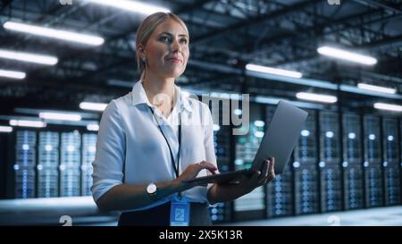 Working Process. Young Creative Caucasian Female Worker Looking Away while Using Laptop Computer in the Dark Evening Office. Businesswoman and e-Business Entrepreneur Concept Stock Photo