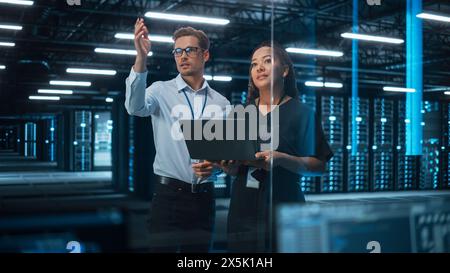 Information Technology Engineer and System Administrator Monitoring Web Services Cloud Solution Software and Sharing Ideas with Each Other in Big Data Center Server. People Use Laptop. Stock Photo
